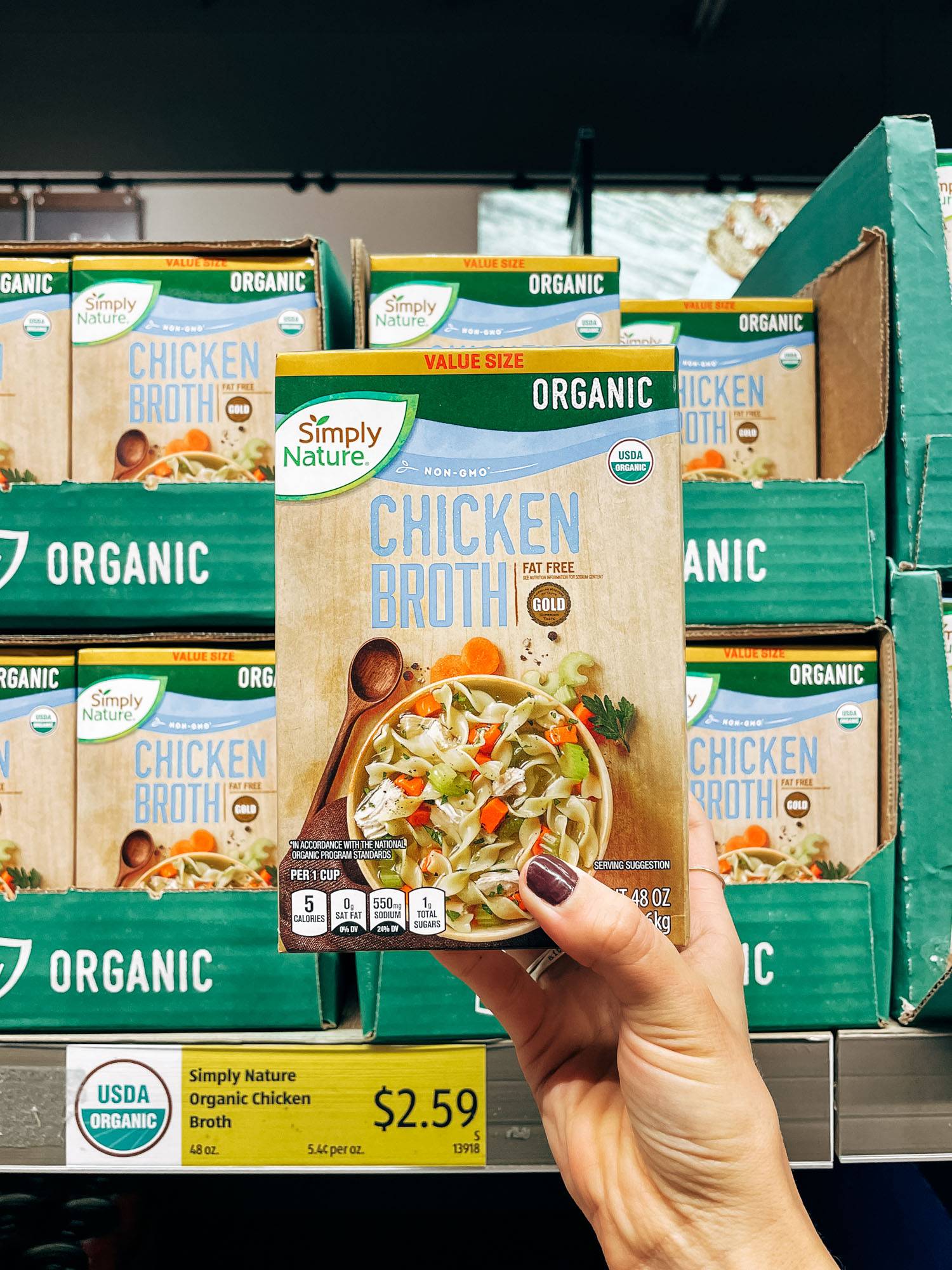 White hand holding a carton of chicken broth