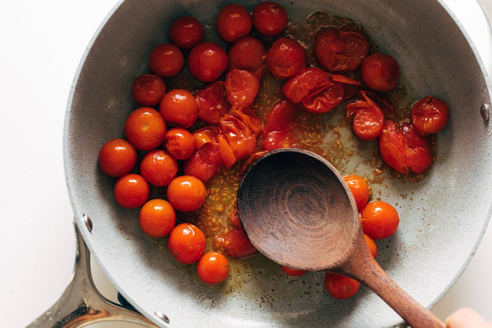 Tomatoes in a pan being smashed with a wooden spoon