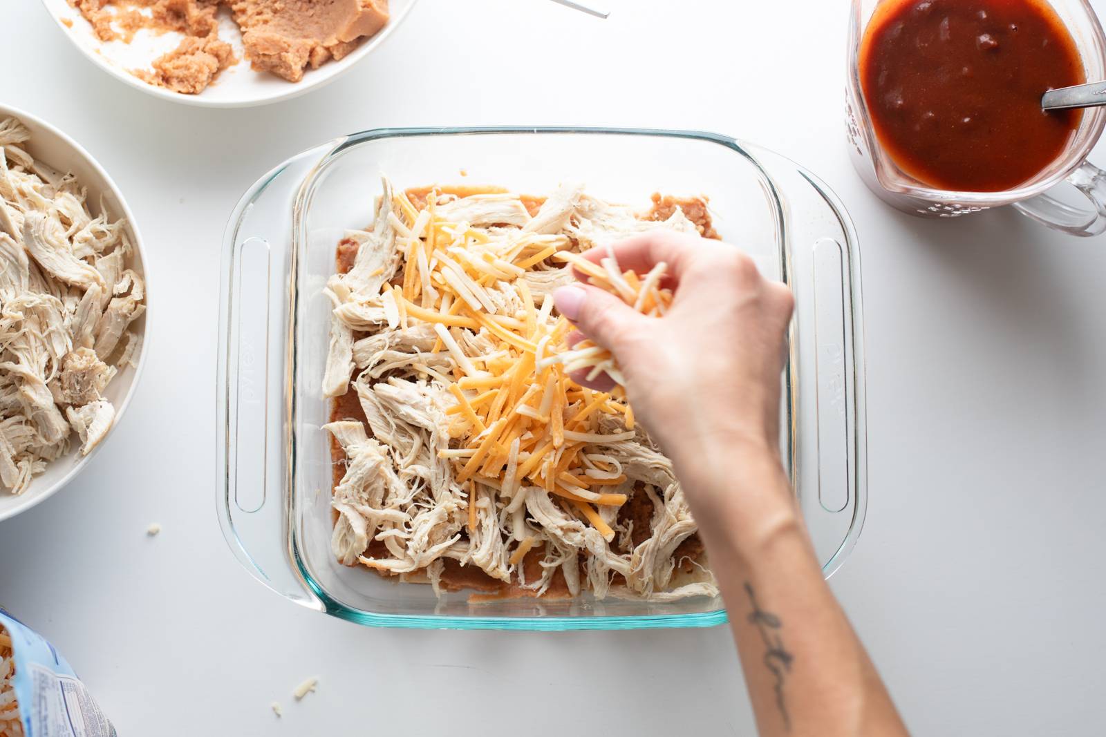 Sprinkling cheese on an enchilada casserole.