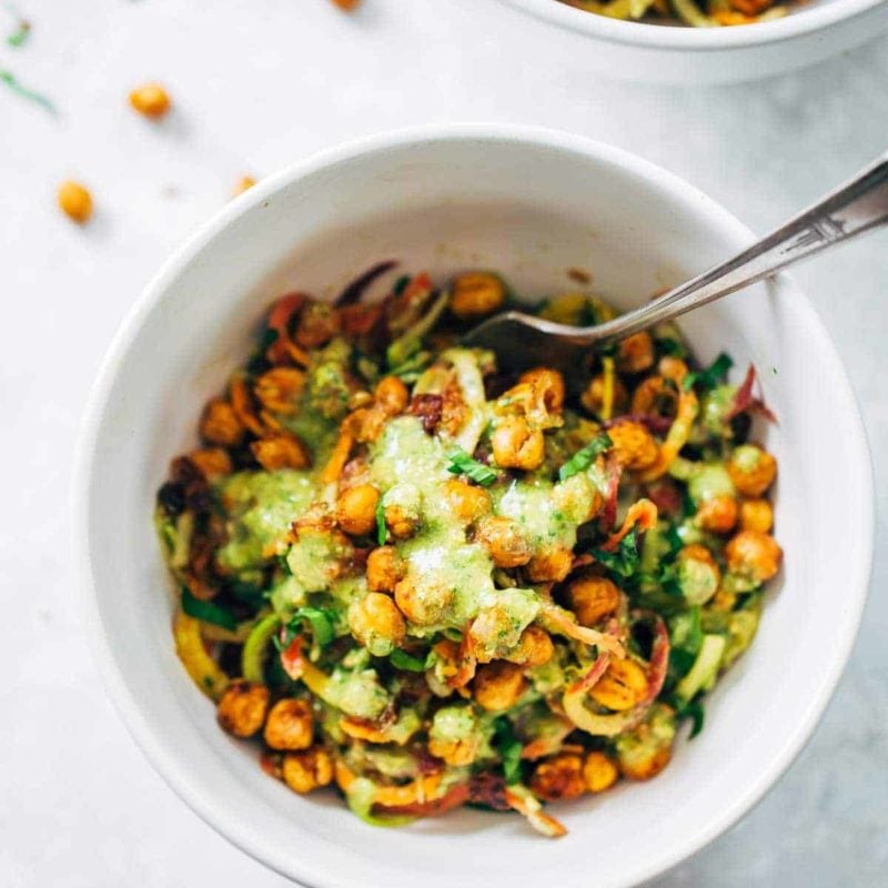 Spiralized veggies in a bowl with chickpeas and green sauce.