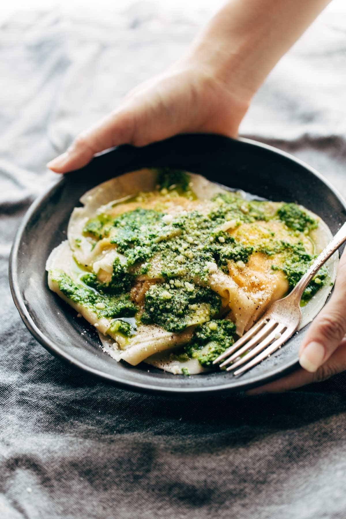 Hand holding Butternut Squash Ravioli on a plate with a fork.